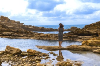 Woman stands barefoot on coastal rock at mount jaizkibel, gazing across the sea while a calm tidal