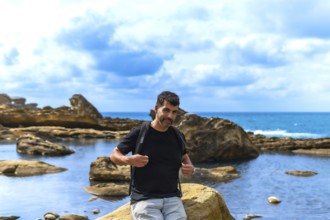 Man with a beard and backpack standing on coastal rocks by the sea, exploring the unique geological