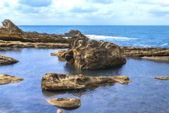 Rocky coastline creating natural tide pools and textured rock formations, showcasing geological