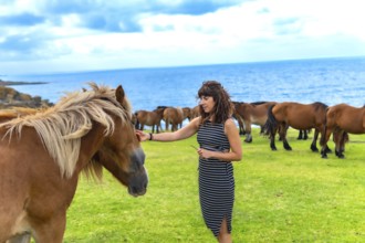Woman interacting with a wild gray horse, gently petting its face while a herd of brown horses