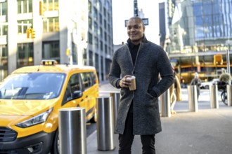 Businessman standing on a new york city street with a coffee cup, a yellow taxi passing in the
