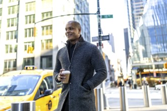 Confident black professional in smart casual coat holding a takeaway coffee cup, walking a busy
