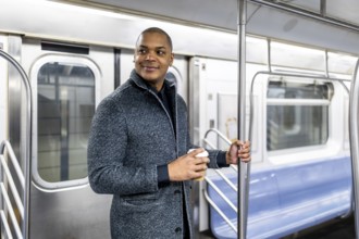 Young businessman traveling by public transport in manhattan, holding a coffee cup and looking