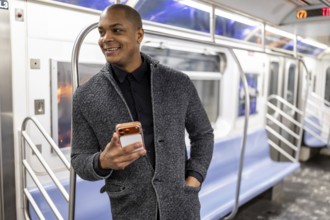 Young african american businessman standing on a subway train in new york city, smiling happily