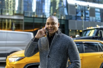 Smiling businessman making a phone call, standing on a busy street in manhattan with cars and