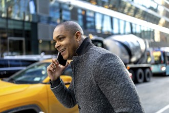 Smiling young executive talks on smartphone while walking a busy manhattan street, surrounded by