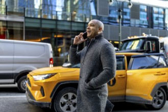 Happy professional businessman talking on a mobile phone, standing on a bustling urban street with