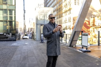 Happy professional man walking and using a smartphone in a bustling manhattan street environment,