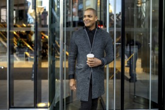 Young black professional man leaving an office building through a modern revolving glass door,