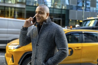 Busy professional man in a winter coat smiling and talking on his smartphone while walking through