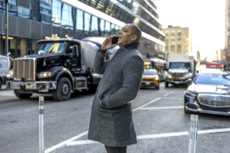 Smiling businessman talking on his mobile while walking a busy manhattan street, illustrating urban