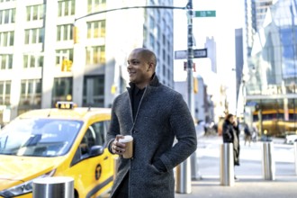 Young man holding a coffee cup, looking thoughtfully while standing on a busy street in manhattan,