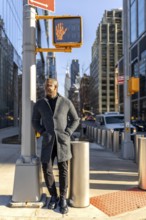 Smiling man standing on a manhattan street at a crosswalk with buildings and traffic in the