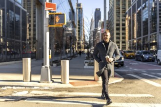 Young businessman walking confidently across a crosswalk in manhattan with a coffee cup, showcasing