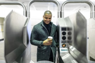 Young professional passing a manhattan subway turnstile with a takeaway coffee, entering the metro
