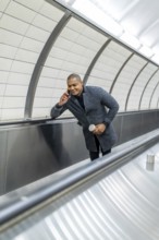 Young businessman traveling on a subway escalator, holding a disposable coffee cup and making a