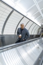 Professional businessman riding a subway escalator in manhattan, holding coffee and smiling as he
