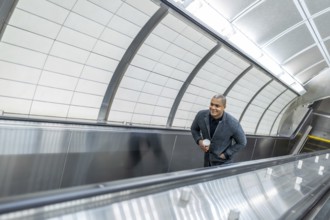 Young businessman ascending a modern escalator in a new york city subway station, holding a coffee
