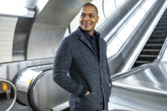 Professional black man smiling, standing confidently on an escalator in a modern subway station,