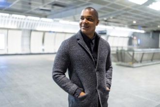 Smiling young african american businessman is standing hands in pockets at a bright, empty subway