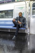 Young african american businessman on a new york city subway, seated with coffee cup, looking out