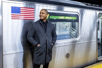 Young african american businessman standing on a subway platform in new york city, smiling while
