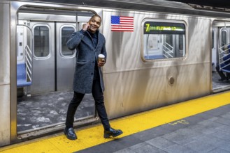 Young professional in a winter coat walks a manhattan subway platform, holding coffee and talking