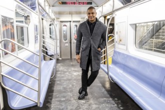 Young man standing inside an empty manhattan subway car, dressing in smart casual attire, smiling