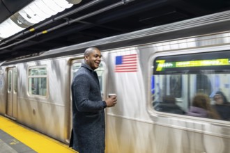 Young businessman standing on a brightly lit subway platform, happily waiting for his train while