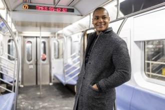 Happy black businessman standing inside an nearly empty new york subway car, smiling as he commutes
