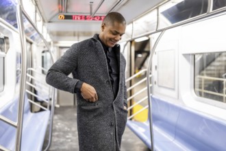 Young professional standing in a manhattan subway car, smiling as he adjusts his coat pocket, ready