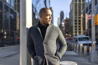Professional man thinking while standing on a busy new york city street, wearing a stylish gray