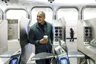 Professional man carrying a coffee cup, about to enter the subway system through modern turnstiles,