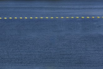 String of yellow cautionary navigation marker buoys on water surafce of river serving to warn,