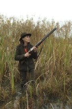 Female hunter standing in water with hunting rifle and eagerly waiting for flying ducks, Allgäu,