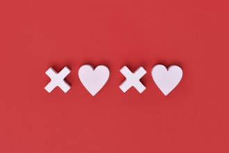 Valentine flat lay with wooden light pink hearts and XOXO letters arranged on a red background.