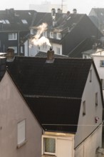 Smoke plume from a chimney over densely built residential area in the evening light, wintry city
