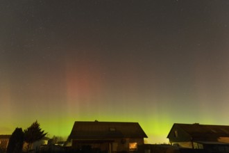 Shimmering red and green auroras over houses under clear starry skies, aurora borealis, Ilsede,
