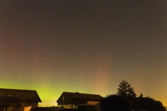 Green and pink polar lights over houses in the evening sky, starry sky, trees at night, aurora