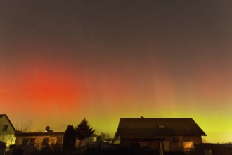Red and green polar lights shine over houses, illuminated night sky, aurora borealis, Ilsede, Lower