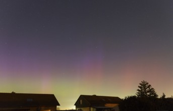 Shimmering purple and green auroras in the evening sky above residential buildings, aurora