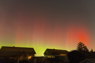 Red-green auroras illuminate the evening sky over residential buildings, aurora borealis, Ilsede,