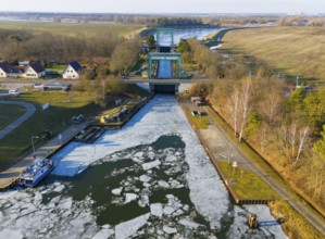 A frozen water surface in front of a lock, with gardens and trees on the edge, aerial view,