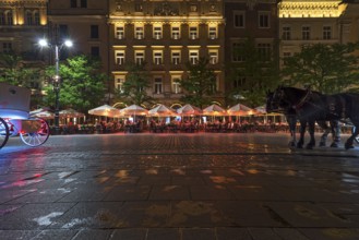Restaurants on the market square at night, horse-drawn carriages left and right, Krakow, Poland