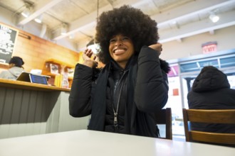 Smiling black woman with a large afro in a warm black puffer jacket sitting in a casual manhattan