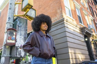 Young woman smiling while standing confidently on a new york city street corner, featuring an afro
