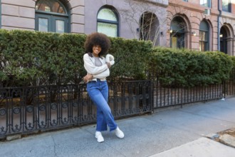 Young black woman with an afro hairstyle smiling confidently while standing on a sidewalk in front