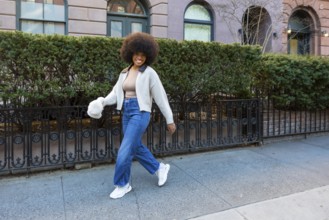 Happy young black woman with afro confidently walking manhattan streets, smiling and enjoying