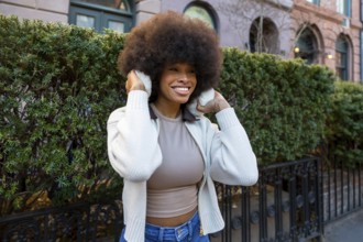African american woman wearing earmuffs and a sweater, smiling brightly while looking away in a