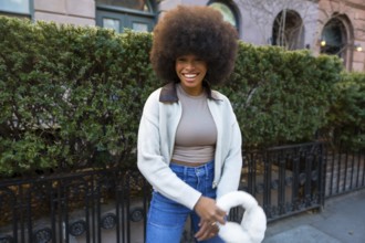 Joyful young black woman with a natural afro hairstyle walking and smiling confidently on a street